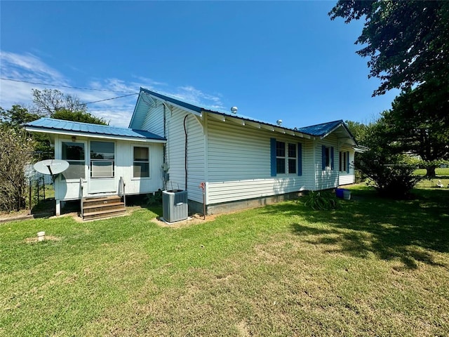 rear view of house with central air condition unit and a lawn