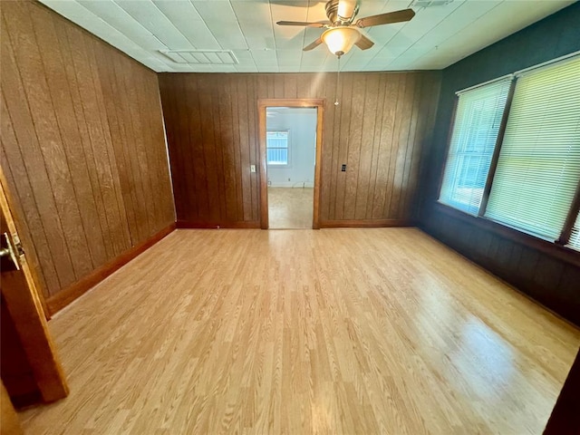 empty room with light wood-type flooring, ceiling fan, and wood walls