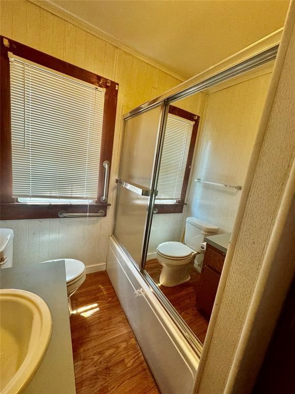 full bathroom featuring enclosed tub / shower combo, wood walls, hardwood / wood-style floors, toilet, and vanity