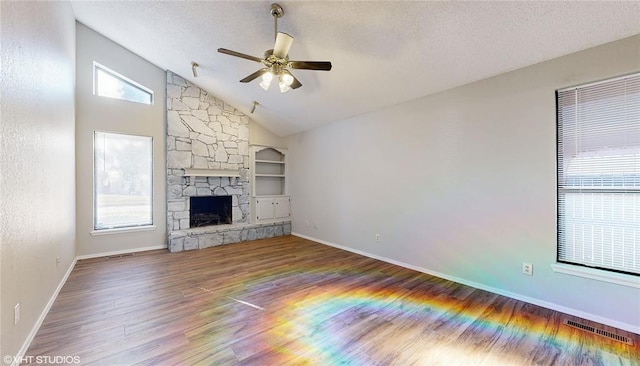 unfurnished living room with hardwood / wood-style flooring, a stone fireplace, ceiling fan, and a healthy amount of sunlight