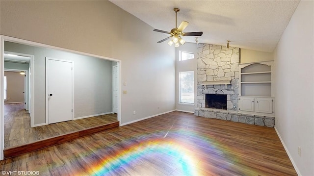 unfurnished living room featuring hardwood / wood-style floors, built in shelves, ceiling fan, and a stone fireplace