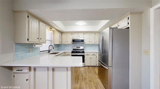 kitchen with a raised ceiling, sink, appliances with stainless steel finishes, light hardwood / wood-style floors, and kitchen peninsula