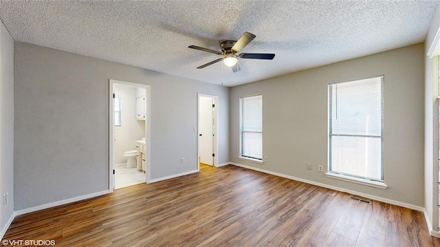 unfurnished bedroom featuring hardwood / wood-style flooring, ensuite bathroom, ceiling fan, and a textured ceiling