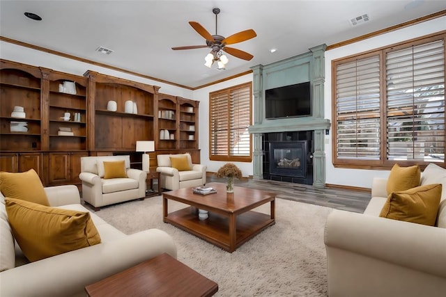 living room featuring plenty of natural light, a tiled fireplace, crown molding, and light hardwood / wood-style flooring