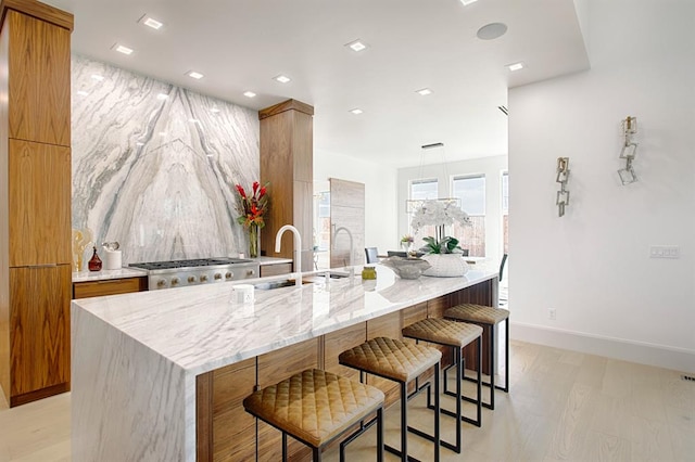 kitchen featuring light stone countertops, sink, stainless steel range oven, light hardwood / wood-style floors, and a kitchen island with sink