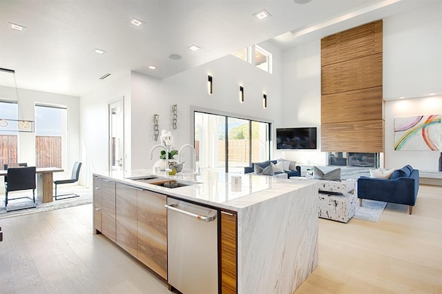 kitchen with a center island with sink, sink, light wood-type flooring, a towering ceiling, and light stone counters