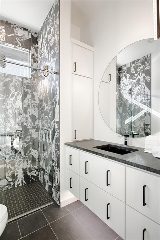 bathroom with toilet, a tile shower, vanity, and tile patterned floors