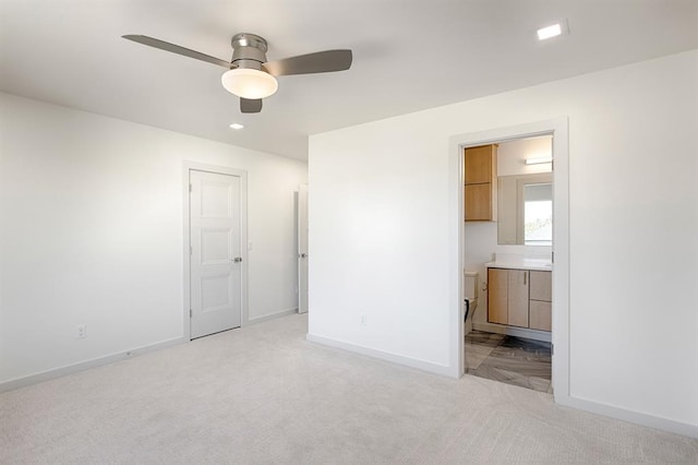 unfurnished bedroom featuring light colored carpet, ensuite bath, and ceiling fan