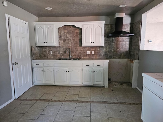 kitchen with white cabinets, tile counters, wall chimney exhaust hood, and sink