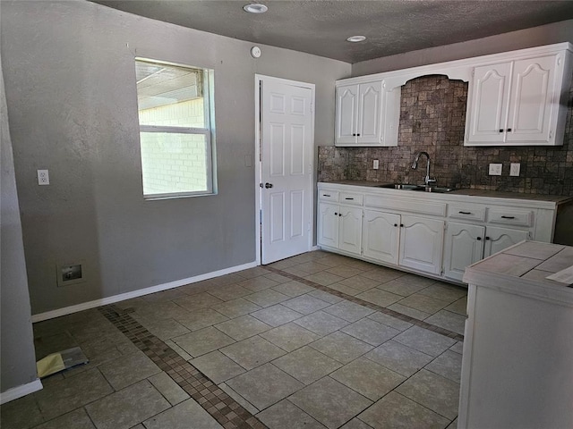 kitchen with decorative backsplash, white cabinetry, sink, and light tile patterned flooring