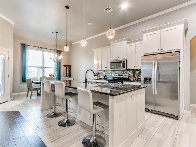 1301 Atalon Dr, Moore, OK 73160 - kitchen with appliances with stainless steel finishes, a center island with sink, a breakfast bar area, white cabinetry, and crown molding