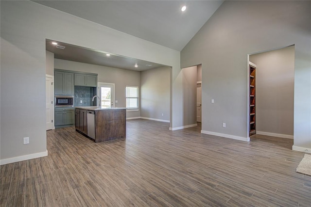 kitchen with a kitchen island with sink, high vaulted ceiling, sink, built in microwave, and wood-type flooring