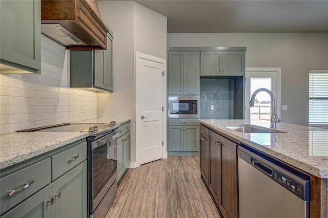 kitchen featuring hardwood / wood-style floors, sink, appliances with stainless steel finishes, tasteful backsplash, and light stone counters