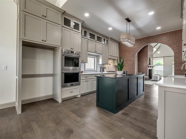 kitchen featuring stainless steel double oven, a healthy amount of sunlight, pendant lighting, and brick wall