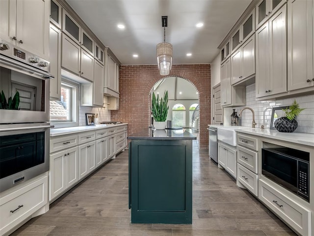 kitchen with brick wall, stainless steel appliances, sink, wood-type flooring, and decorative light fixtures