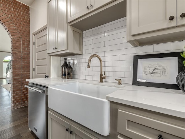 kitchen featuring dark wood-type flooring, sink, stainless steel dishwasher, decorative backsplash, and light stone countertops