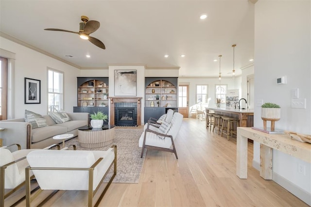 living room featuring sink, crown molding, ceiling fan, a fireplace, and light hardwood / wood-style floors