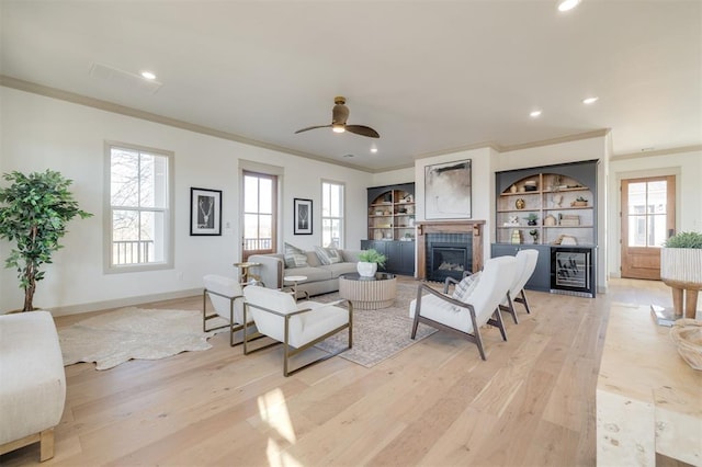 living room featuring a tiled fireplace, ceiling fan, ornamental molding, and light wood-type flooring