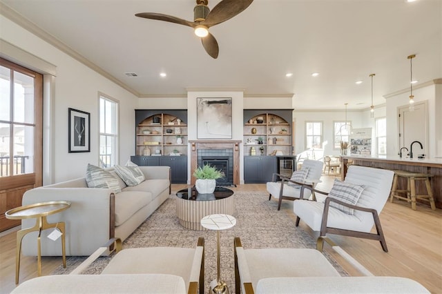 living room with a tile fireplace, sink, crown molding, ceiling fan, and light hardwood / wood-style floors