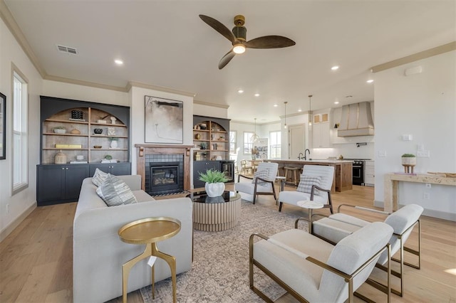 living room with a tile fireplace, sink, ceiling fan, light wood-type flooring, and ornamental molding