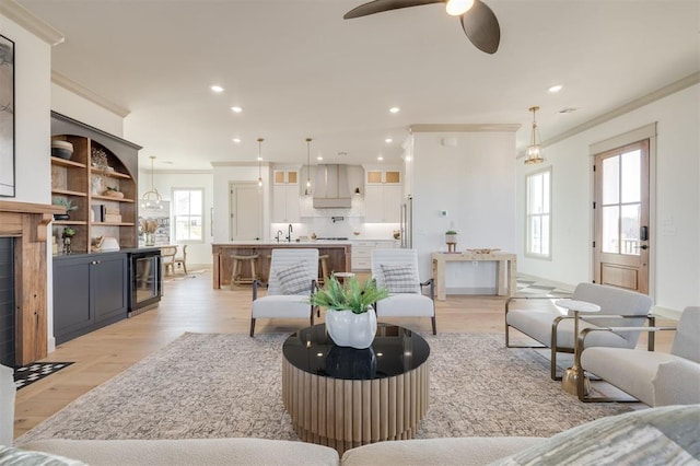 living room with beverage cooler, light hardwood / wood-style floors, ceiling fan, and ornamental molding