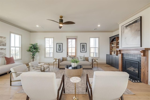 living room featuring a fireplace, light wood-type flooring, ceiling fan, and ornamental molding