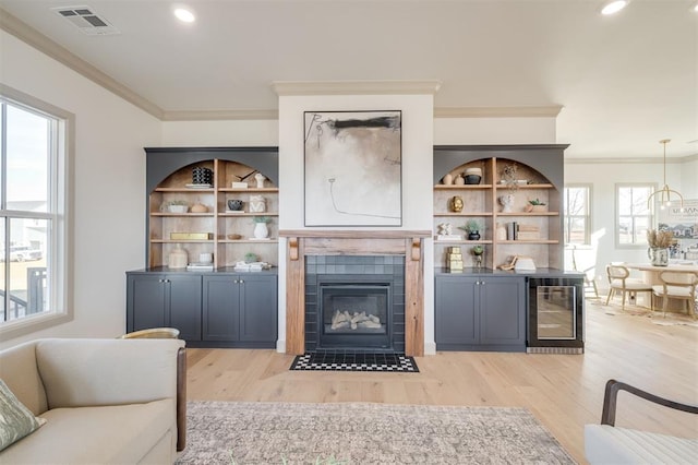 living room with a tiled fireplace, beverage cooler, light hardwood / wood-style floors, and ornamental molding