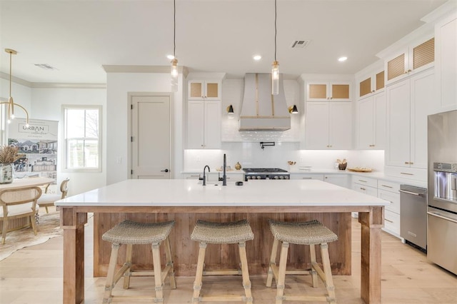 kitchen with pendant lighting, appliances with stainless steel finishes, wall chimney exhaust hood, and an island with sink