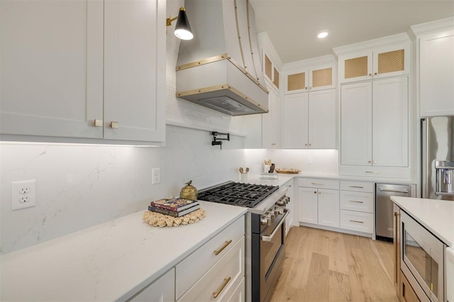 kitchen featuring decorative backsplash, custom range hood, stainless steel appliances, light hardwood / wood-style floors, and white cabinetry