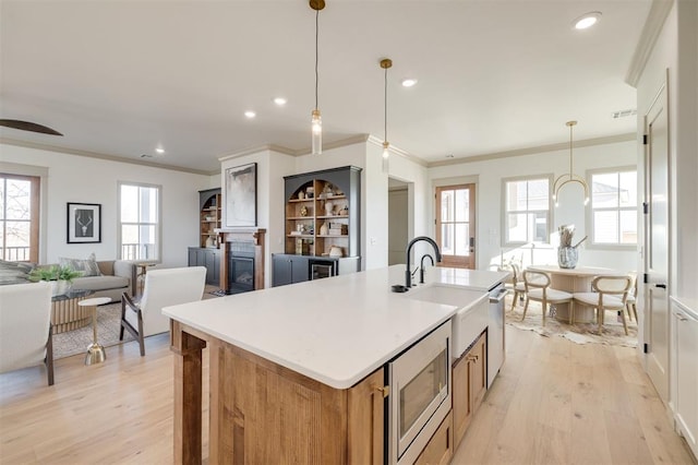 kitchen featuring a kitchen island with sink, light wood-type flooring, ornamental molding, decorative light fixtures, and stainless steel appliances