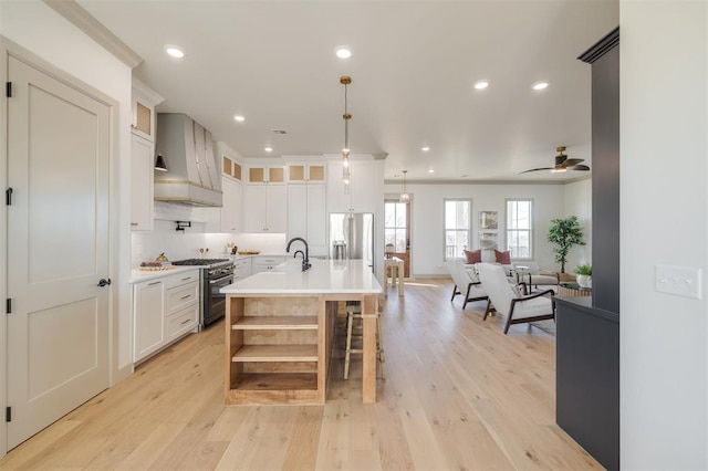 kitchen featuring white cabinetry, wall chimney exhaust hood, hanging light fixtures, appliances with stainless steel finishes, and light wood-type flooring