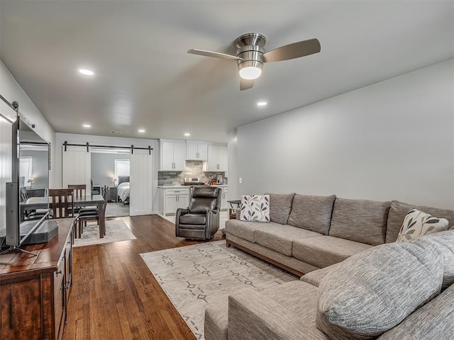 living room with a barn door, ceiling fan, and dark wood-type flooring