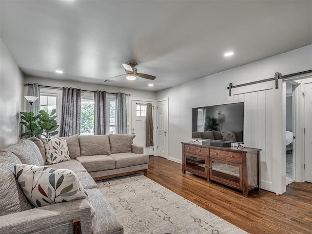 living room featuring ceiling fan, a barn door, and wood-type flooring