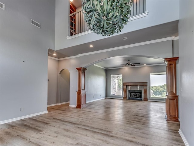 unfurnished living room featuring ornate columns, ceiling fan, a towering ceiling, light hardwood / wood-style floors, and a fireplace