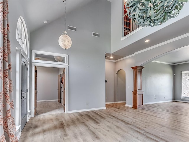 unfurnished living room featuring ornate columns, light hardwood / wood-style flooring, high vaulted ceiling, and ornamental molding