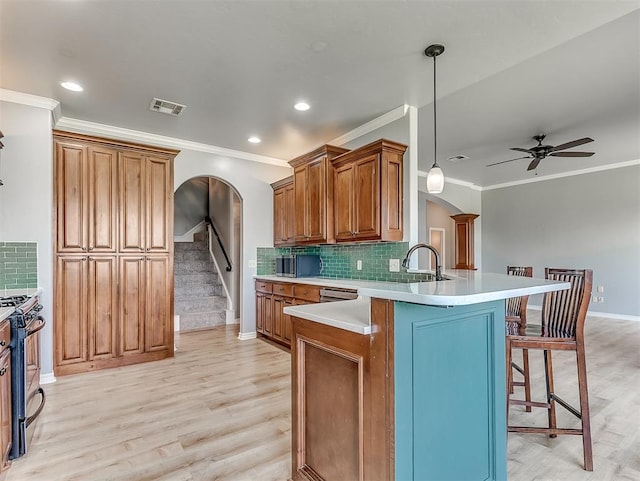 kitchen with decorative backsplash, black range with gas stovetop, crown molding, decorative light fixtures, and light hardwood / wood-style flooring