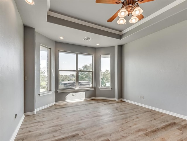 spare room featuring light wood-type flooring, a tray ceiling, ceiling fan, and crown molding