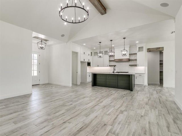 kitchen with tasteful backsplash, a chandelier, hanging light fixtures, a center island with sink, and white cabinets