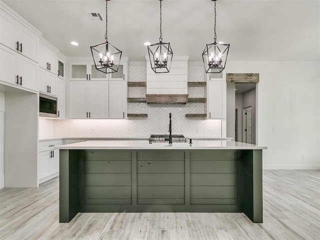 kitchen featuring hanging light fixtures, a kitchen island with sink, and white cabinets