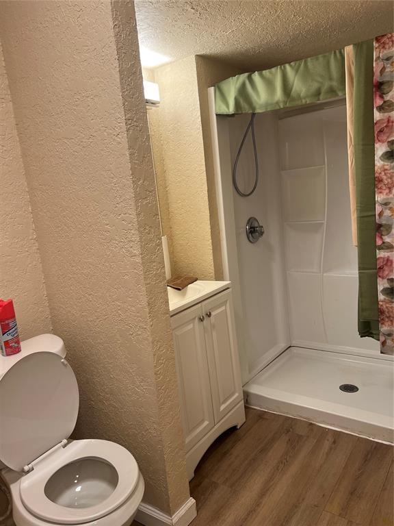 bathroom featuring walk in shower, a textured ceiling, vanity, hardwood / wood-style flooring, and toilet