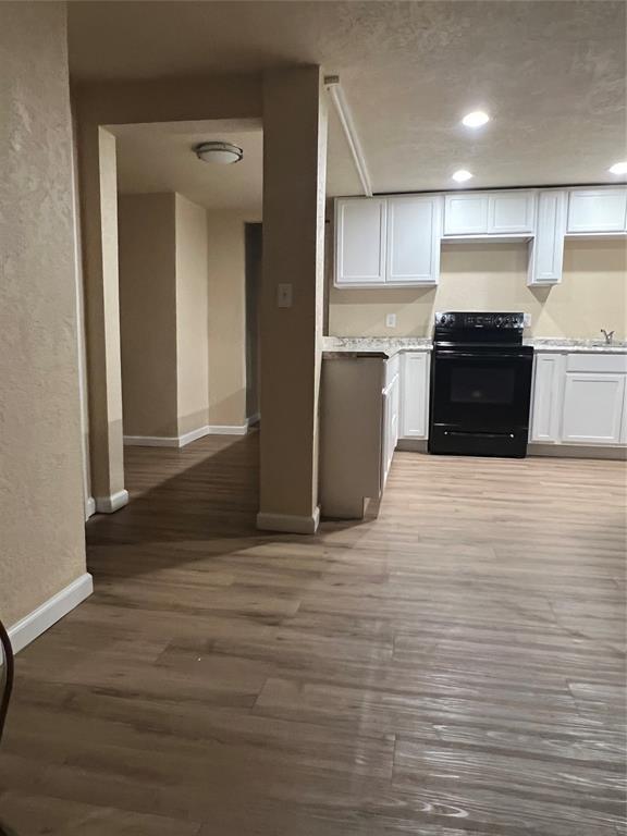 kitchen with black range with electric stovetop, white cabinets, and hardwood / wood-style flooring