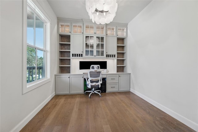 unfurnished office featuring hardwood / wood-style floors, built in desk, and a notable chandelier