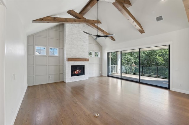 unfurnished living room featuring hardwood / wood-style floors, beam ceiling, a stone fireplace, and high vaulted ceiling