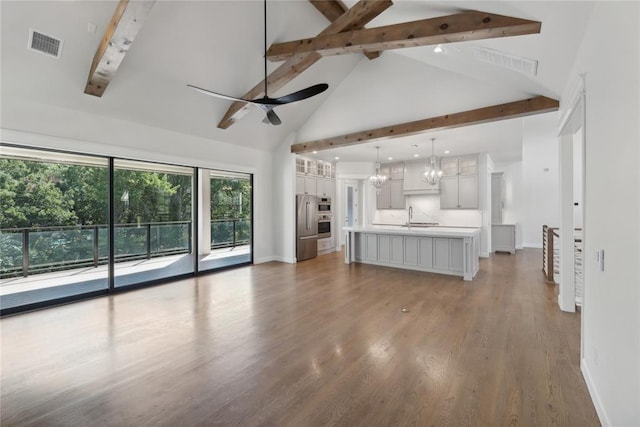 unfurnished living room featuring ceiling fan with notable chandelier, dark wood-type flooring, sink, beam ceiling, and high vaulted ceiling