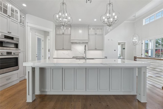 kitchen featuring a large island with sink, decorative light fixtures, and double oven