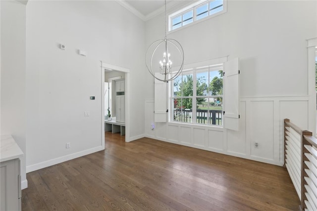 unfurnished living room featuring a towering ceiling, dark hardwood / wood-style floors, a wealth of natural light, and crown molding