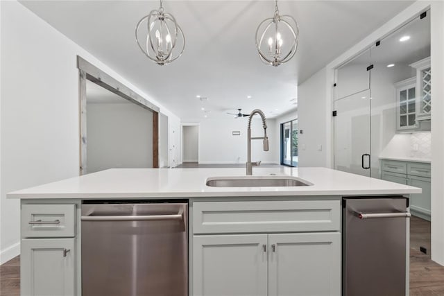 kitchen with a kitchen island with sink, dark wood-type flooring, ceiling fan with notable chandelier, sink, and stainless steel dishwasher