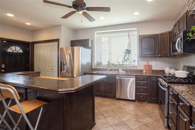 kitchen featuring light tile patterned floors, a kitchen bar, ceiling fan, appliances with stainless steel finishes, and sink