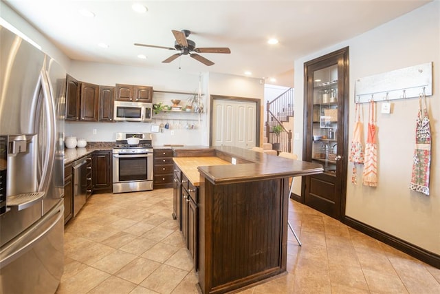 kitchen featuring ceiling fan, a kitchen island, light tile patterned flooring, dark brown cabinetry, and appliances with stainless steel finishes