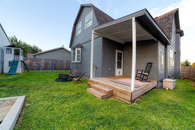 rear view of property with a deck, an outdoor fire pit, and a lawn